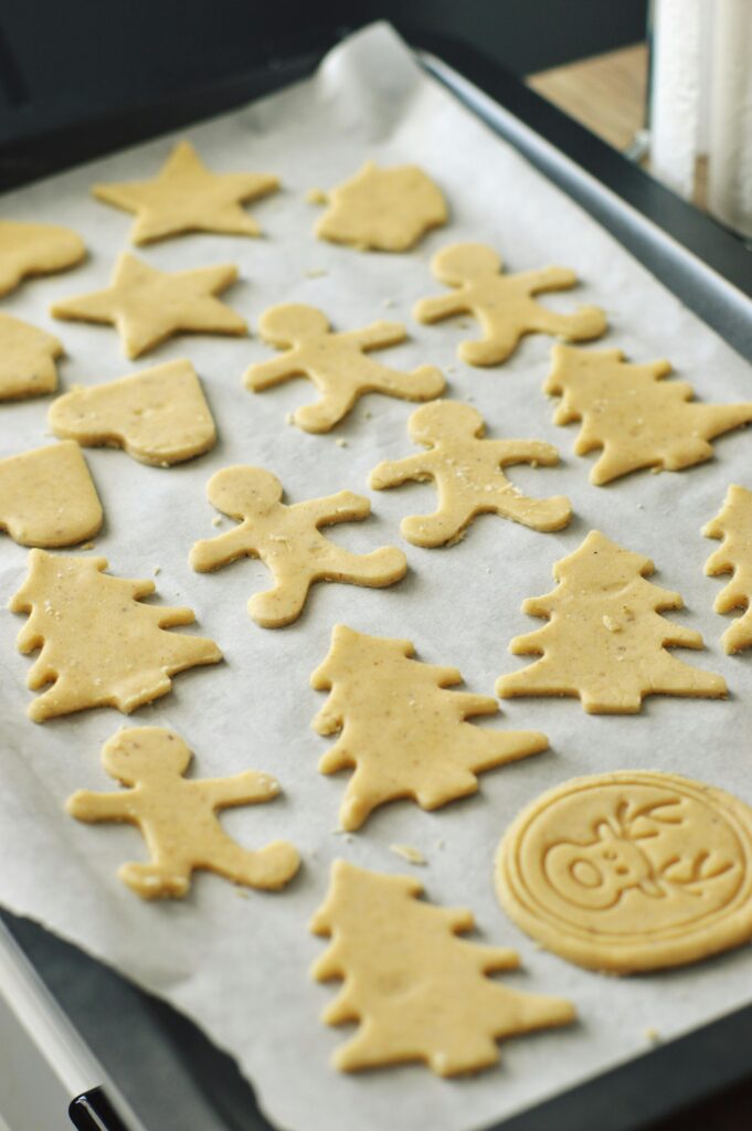 Raw festive holiday cookie dough shapes on parchment paper ready for baking.